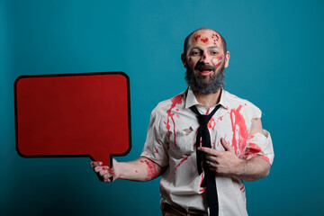 Scary monster holding mockup speech bubble, showing text message on isolated copyspace carton. Brain eating creepy zombie with scars and bloody wounds doing advertisement in studio.