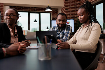African american colleagues brainstorming ideas in office, using laptop and tablet to create online presentation with data research and information. Analyzing documents to send email report.