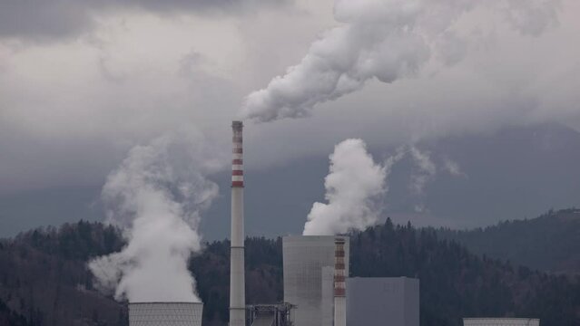The heavy gray sky over thermal power plant smokestacks that blow out smoke and smog, burning coal polluting the air