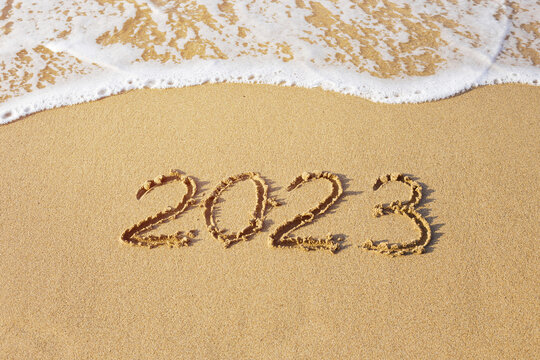 New year concept photo. Numbers 2023 handwritten on a sand beach. Frothy wave on background.