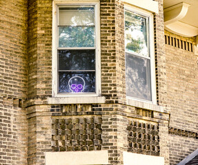 A neon white and purple skull in the window of an ornate brick building.