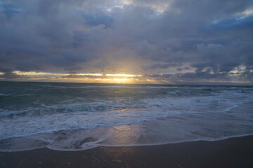 dark clouds of a storm under which sunbeams of the sunset shine on the sea seen from the beach, North Sea