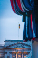 Royal Standard flag flies above Buckingham Palace at dusk framed by a union flag on a pole - Medium 