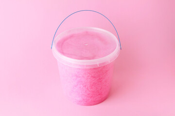close up sweet fluffy pink color cotton candy in plastic basket package on pink background. spun...