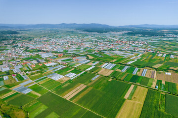 Fototapeta na wymiar Panoramic view of large greenhouses and fields and houses. Flight over large industrial greenhouses on a sunny day.