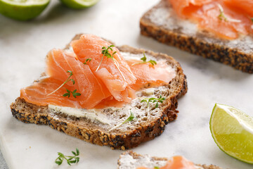 Wholewheat bread sandwiches with cream cheese and smoked salmon on marble board with lime slices...