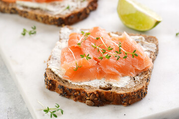 Wholewheat bread sandwiches with cream cheese and smoked salmon on marble board with lime slices and sour cream