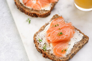 Wholewheat bread sandwiches with cream cheese and smoked salmon on marble board with lime slices and sour cream