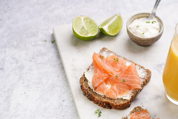 Wholewheat bread sandwiches with cream cheese and smoked salmon on marble board with lime slices...