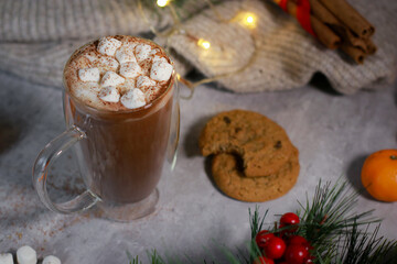 hot chocolate in a glass mug with mini marshmallows on grey table, blurred xmas background 