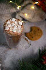 top view of hot chocolate in a glass mug with mini marshmallows on grey table, blurred xmas background 