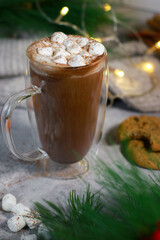 hot chocolate in a glass mug with mini marshmallows on grey table, blurred xmas background 