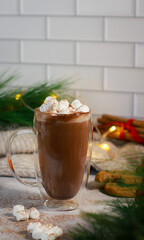 hot chocolate in a glass mug with mini marshmallows on grey table, blurred xmas background 