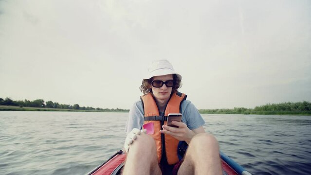 A young man is kayaking on the river against the backdrop of a beautiful landscape and taking pictures on his phone. Travel. Tourism.