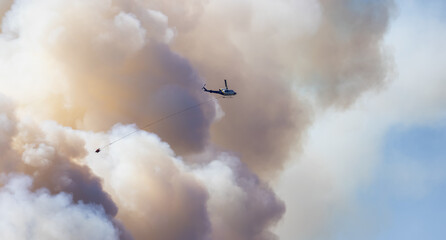 Wildfire Service Helicopter flying over BC Forest Fire and Smoke on the mountain near Hope during a hot sunny summer day. British Columbia, Canada. Natural Disaster