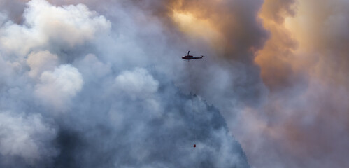 Wildfire Service Helicopter flying over BC Forest Fire and Smoke on the mountain near Hope during a hot sunny summer day. British Columbia, Canada. Natural Disaster