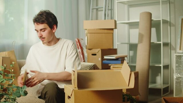 Moving to new house. Real estate, buying flat apartment. Young man wrapping things in cardboard boxes, guy owner during relocation. Property purchasing. Housing service concept.