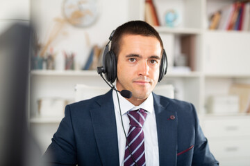 Office worker man is working at computer and talking by headset with client in the office