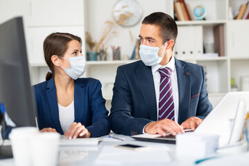 Confident male and female business partners wearing protective masks working in office. New standards due to coronavirus outbreak