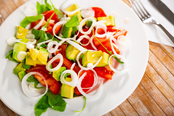 Traditional vegetarian salad from fresh ripe avocado with tomatoes, sliced onions and greens dressed with oil