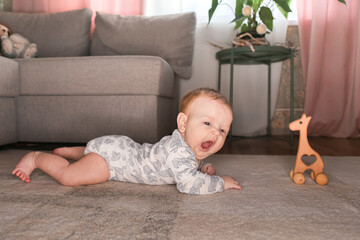 a small child, a baby in a bodysuit lies in the living room on the floor, on the carpet, plays with wooden toys, lifestyle, childhood, baby care, eco-friendly toys, early development