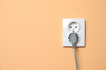 Double power socket with inserted plug on pale orange wall, space for text. Electrical supply