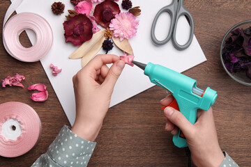 Woman using hot glue gun to make craft at wooden table, top view