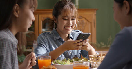 Asia young smart casual girl group friend sit at indoor coffee shop table enjoy laugh fun eat food drink lunch meal party at cafe. Relax look read e-mail text, money trade or post IG reel story app.