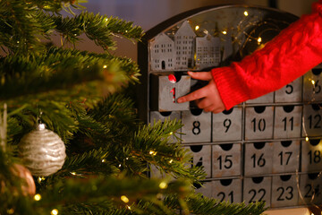 advent calendar.A child hand in a red sweater opens the advent calendar near Christmas tree with...