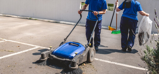Two young latino janitorial workers (man and woman) in uniform cleaning in parking lot with outdoor industrial vacuum cleaner