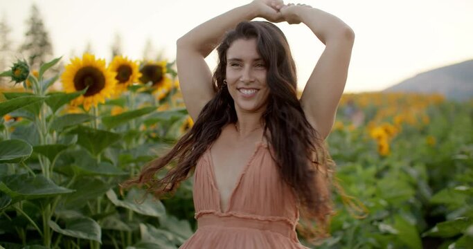 Happy, young beautiful girl spins in sun dress in sunflower field
