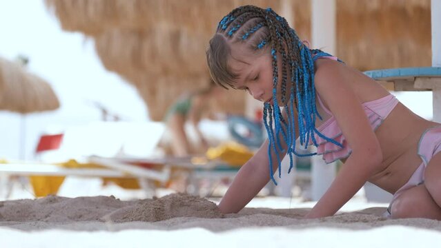 Pretty child girl in bikini swimsuit playing with sand in umbrella shadow during summer tropical vacation