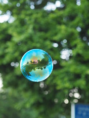 Soap bubble flying in the air reflecting green garden