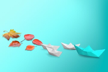 Paper boat with fresh tree leaves on blue background.