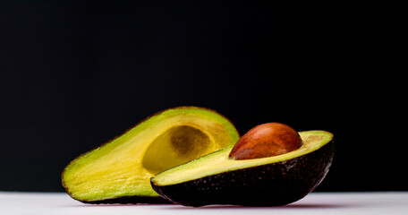 The front corner of the avocado, cut in half, shows off the yellow and green flesh inside. placed...