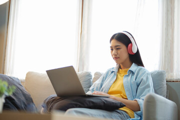 Naklejka premium Young asian woman studying and listening to music while sitting on couch at home.