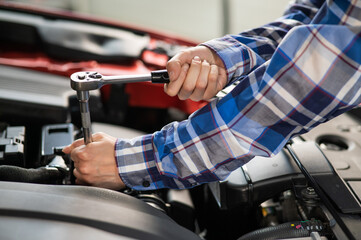 Female auto mechanic unscrewing a nut to replace a car spark plug.