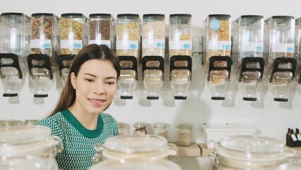 Young Caucasian female customer is choosing and shopping for organic products in refill store with reusable bag, zero-waste grocery, and plastic-free, eco environment-friendly, sustainable lifestyles.