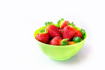 Green bowl on a white surface full of beautiful strawberries.