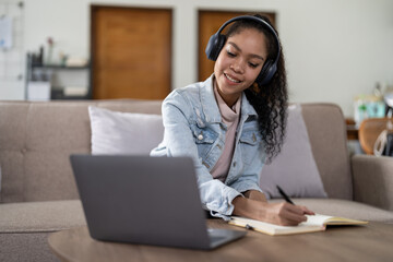 mixed race woman wearing headphones watching webinar write notes study online with online teacher, african female student learning language computer course on laptop listen translate lecture