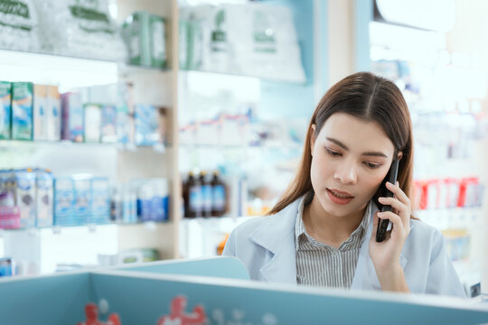 A Female Pharmacist Checks Drug Stocks In A Community Pharmacy. Use The Phone To Talk