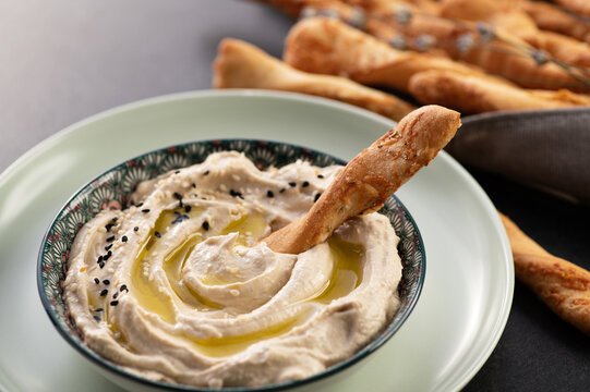 Classic hummus, ready-made dish decorated with sesame seeds, served with grisini breadsticks, close-up