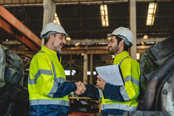 Caucasian factory engineer talking and shaking hands on business cooperation agreement. Successful hand shaking after good deal, workers handshaking each other at heavy industrial production line.