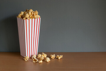Striped box with popcorn on wooden table and grey background with space for text.