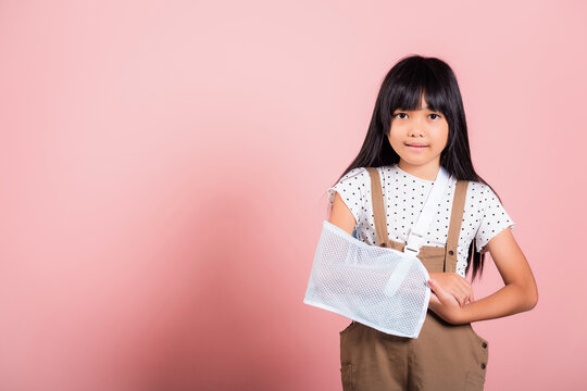 Arm broken. Asian little kid 10 years old hand bone broken from accident with arm splint at studio shot isolated on pink background, Happy child girl accident insurance and extreme sports speed