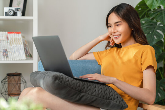 Cheerful young woman wear orange shirt with sitting on sofa and using laptop computer at home.
