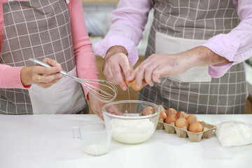 Obraz na płótnie Canvas Happy young couple multiethnic man and woman hands making homemade bakery cake, pouring milk while breaking eggs and mixing flour into glass bowl in the kitchen. Family having fun while prepare food