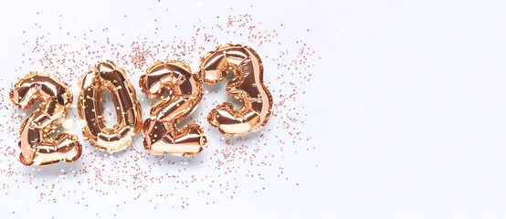 Banner with 2023 golden foil balloons and crystals confetti on a blue background. Festive concept...