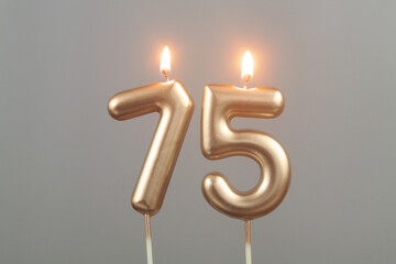 Burning gold birthday candles on gray background, number 75