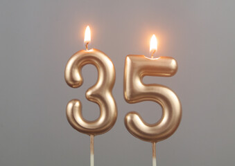 Burning gold birthday candles on gray background, number 35